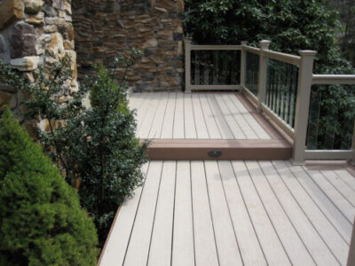 Deck Builder Ladue, MO Two-level deck with railing attached to stone house and surrounded by trees and shrubs